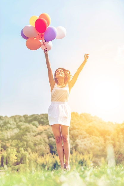 S'envoler. Heureuse jeune femme tenant des ballons colorés et volant au-dessus d'un pré vert