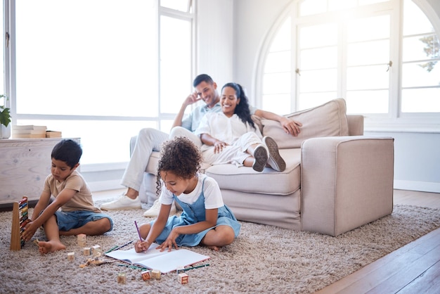 S'occuper à sa manière. Plan de deux petits frères et sœurs jouant avec des jouets et écrivant dans un livre pendant que leurs parents se détendent sur un coffre-fort dans le salon à la maison.