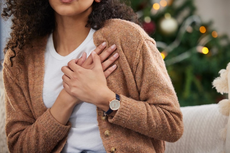 Photo sa poitrine est un peu serrée photo recadrée d'une jeune femme méconnaissable tenant sa poitrine dans la douleur alors qu'elle était assise sur son canapé à noël