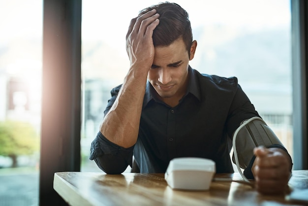 Sa tension artérielle augmente Photo d'un jeune homme d'affaires vérifiant sa tension artérielle dans un bureau