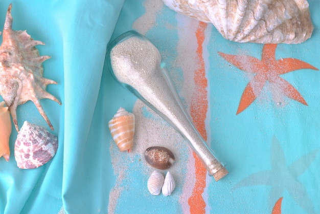 Sable dans une petite bouteille et coquillages tropicaux sur une serviette de plage