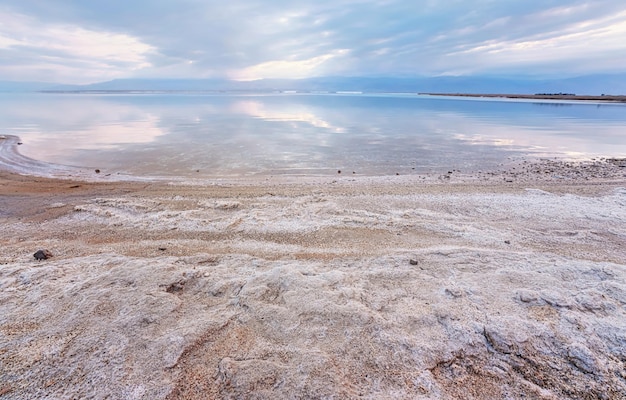 Sable et pierres recouvertes de sel cristallin sur les rives de la mer Morte, eau calme et claire à proximité - paysage typique de la plage d'Ein Bokek, Israël