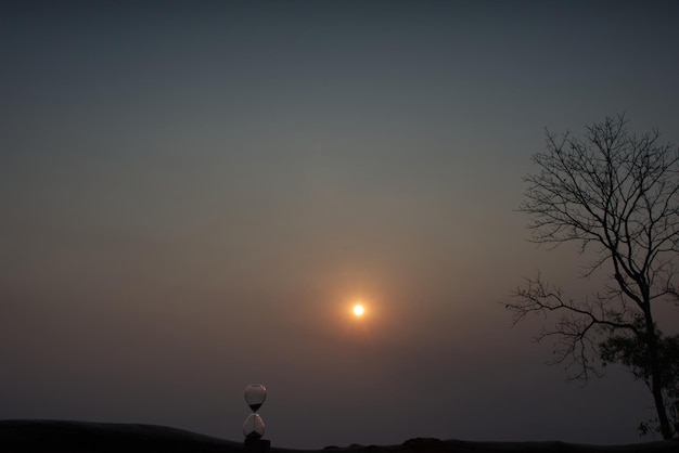 Un sablier avec du sable qui tombe avec une mer de brouillard et une silhouette de chaîne de montagnes à l'heure du lever du soleil