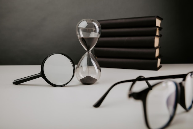 Sablier avec loupe de lunettes et livres sur une table