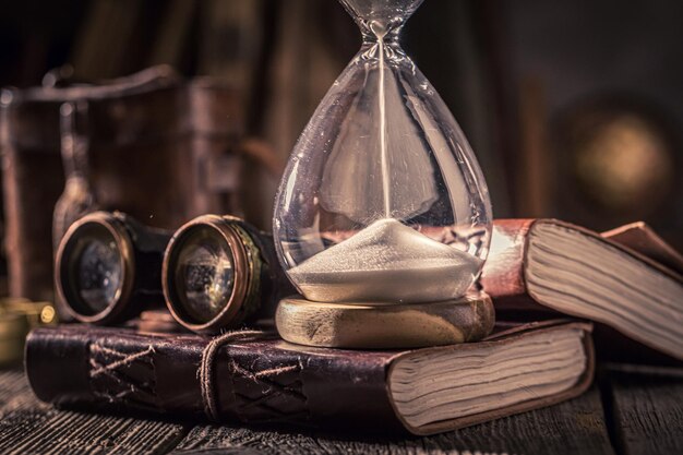 Photo sablier vieilli et journal avec livres binoculaires et boussole