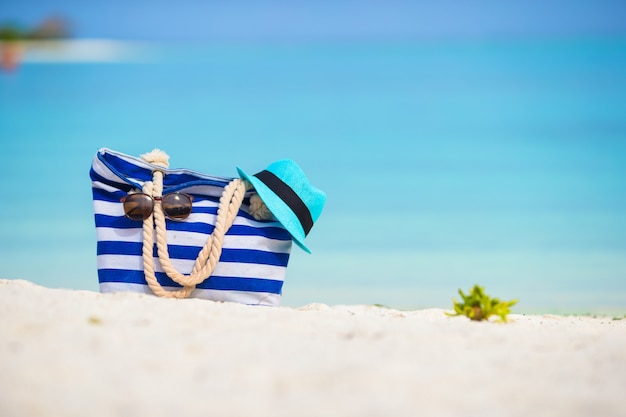 Sac bleu, chapeau de paille, lunettes de soleil sur la plage blanche