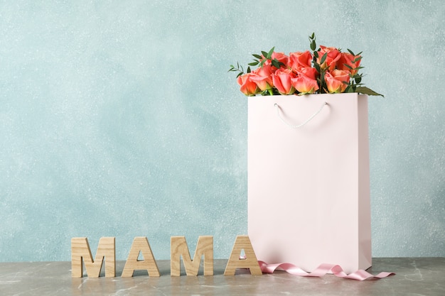 Sac cadeau avec bouquet de roses roses et inscription maman sur table grise