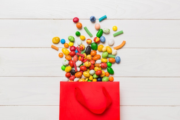 Sac cadeau en papier commercial dans un coin plein de bonbons traditionnels assortis tombant sur fond coloré avec espace de copie Concept de vente Joyeuses Fêtes