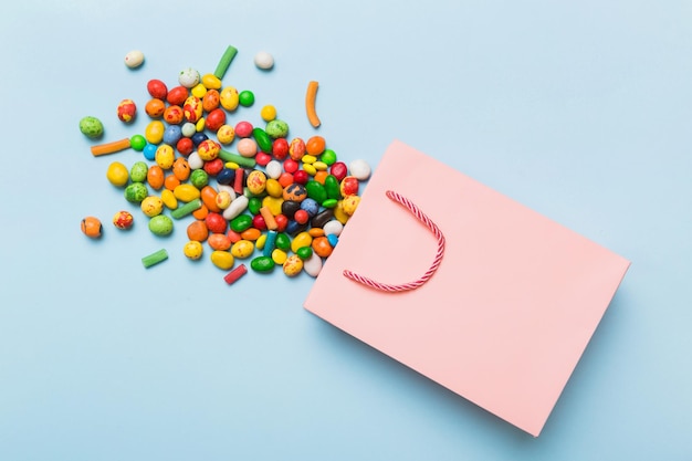 Sac cadeau en papier commercial dans un coin plein de bonbons traditionnels assortis tombant sur fond coloré avec espace de copie Concept de vente Joyeuses Fêtes