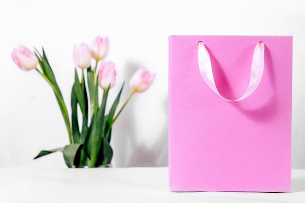 Un sac cadeau rose avec de délicates fleurs de tulipes sur fond blanc Remises et soldes