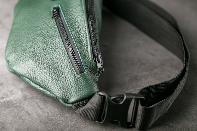 Sac ceinture en cuir texturé vert foncé, banane sur une table grise.