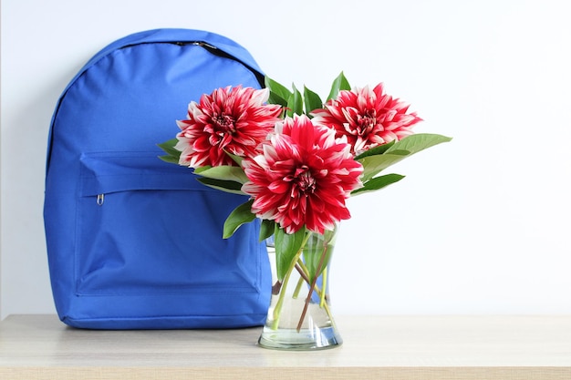 Un sac à dos bleu et des dahlias rouges