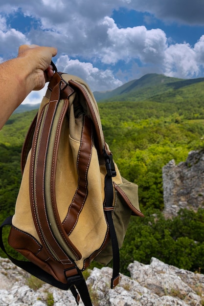 Un sac à dos brun-vert entre les mains d'un homme sur fond de montagnes verdoyantes Le concept d'un mode de vie actif