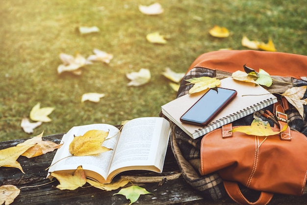 Le Sac à Dos Est Placé Sur Une Table En Bois Antique Avec Des Livres, Des Cahiers, Des Téléphones Et La Nature Des Feuilles D'érable Depuis La Vue De Dessus.