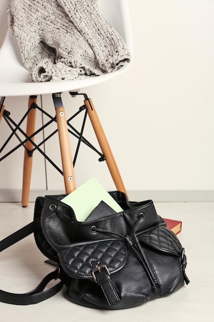 Photo sac à dos femme mode avec livre près d'une chaise blanche sur un sol