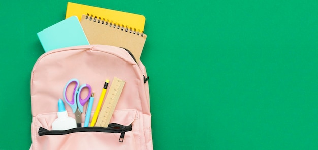 Sac à dos avec fournitures de bureau qui en sort sur fond vert