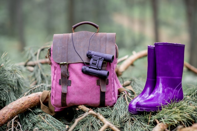 Photo sac à dos avec jumelles et bottes en caoutchouc dans la pinède. concept de voyage