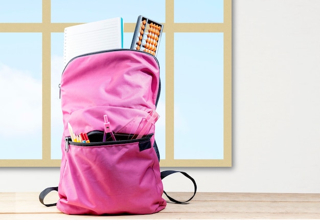 Sac à dos avec livre et stationnaire sur une table en bois avec un fond en verre de fenêtre. Concept de retour à l'école