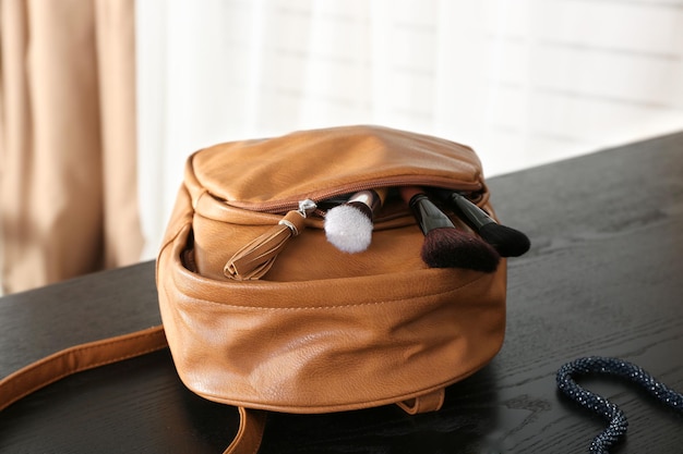 Sac à dos avec pinceaux de maquillage et vernis à ongles sur table en bois à l'intérieur