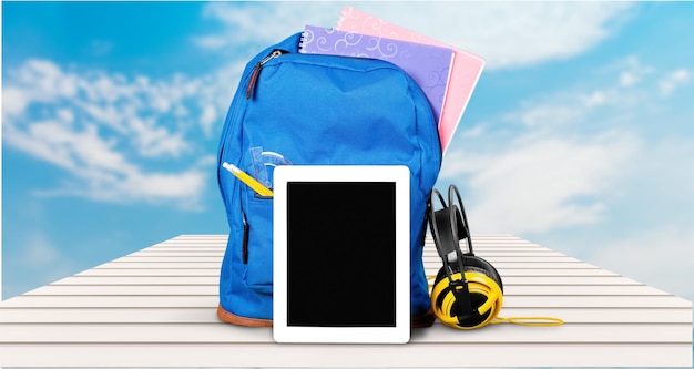 Sac à dos scolaire bleu avec tablette et écouteurs en arrière-plan.