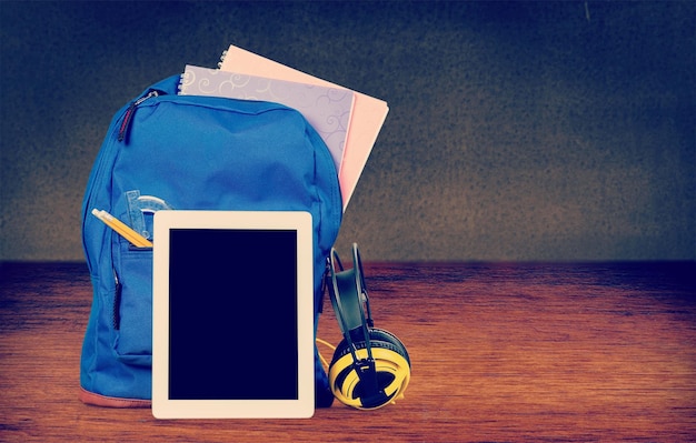 Sac à dos scolaire bleu avec tablette et écouteurs sur fond de classe