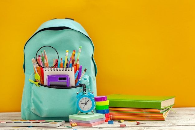 Sac à dos scolaire complet avec différentes fournitures sur fond orange.