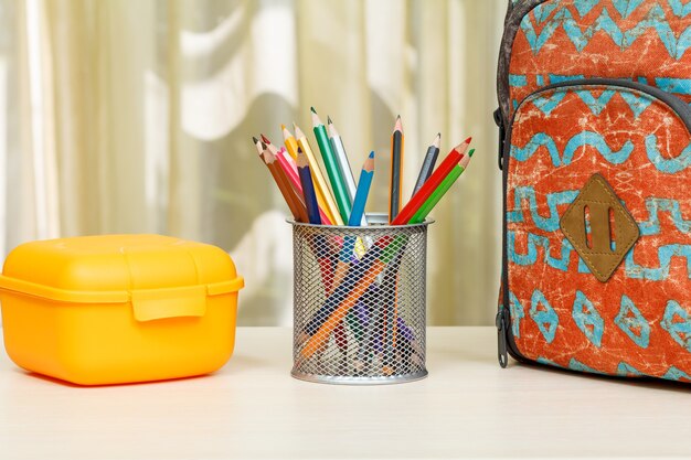 Photo sac à dos scolaire avec fournitures scolaires. support en métal pour crayons avec crayons de couleur et boîte à sandwich jaune sur table en bois. retour au concept de l'école.