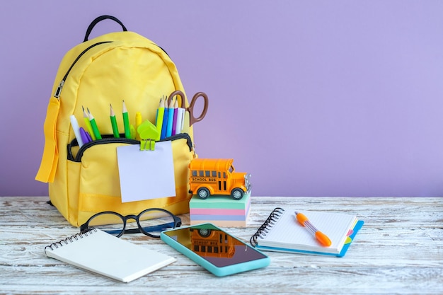 Sac à dos scolaire jaune complet avec papeterie sur table sur fond violet.