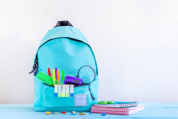 Sac à dos scolaire turquoise avec papeterie sur table.