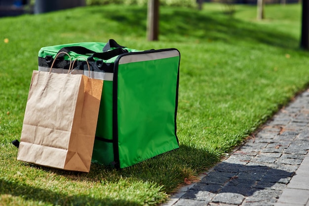 Sac à dos thermique vert et sac en papier avec de la nourriture debout sur l'herbe verte à l'extérieur