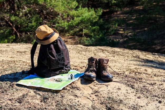 Sac à dos touristique avec chaussures de randonnée, chapeau, boussole et carte sur la clairière dans la forêt de pins. Matériel de randonnée trekking. Notion de voyage