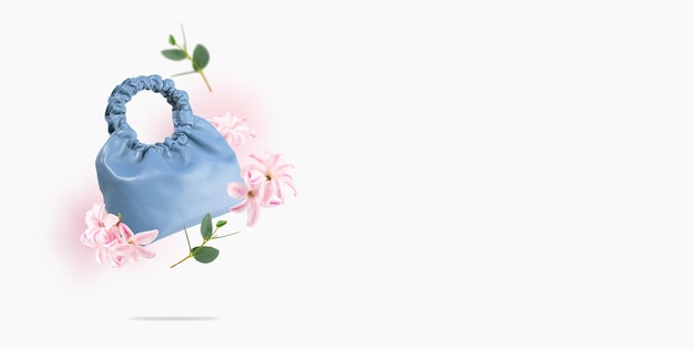 Un sac en écocuir bleu laisse des fleurs flotter sur un fond grisComposition créative de sac en cuir fait main volant et de fleursConcept d'accessoires pour femmes de printemps et d'été Espace de copie de la bannière