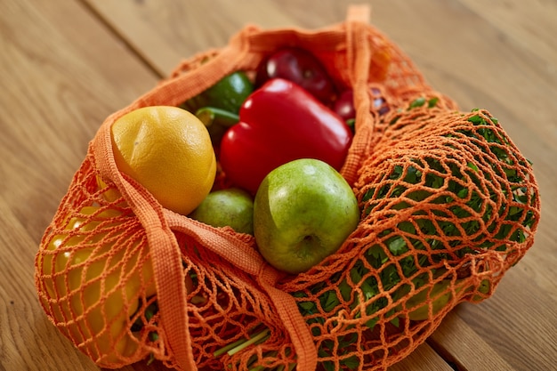 Sac écologique en maille d'achat avec des légumes et des fruits végétaliens sains dans la cuisine à la maison, concept végétarien d'alimentation saine.