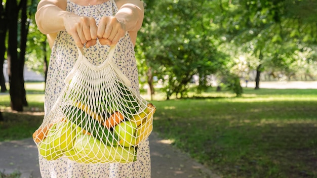 Sac en filet tricoté avec des légumes et des fruits entre les mains d'une femme