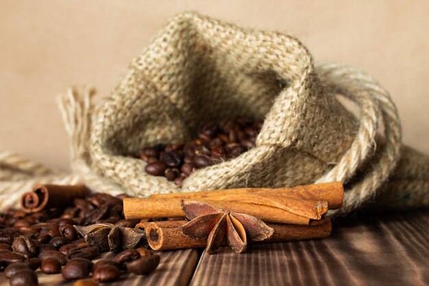 Sac de jute grossier avec des grains de café saupoudrés sur une table en bois brûlé avec des bâtons de cannelle et des étoiles d'anis.