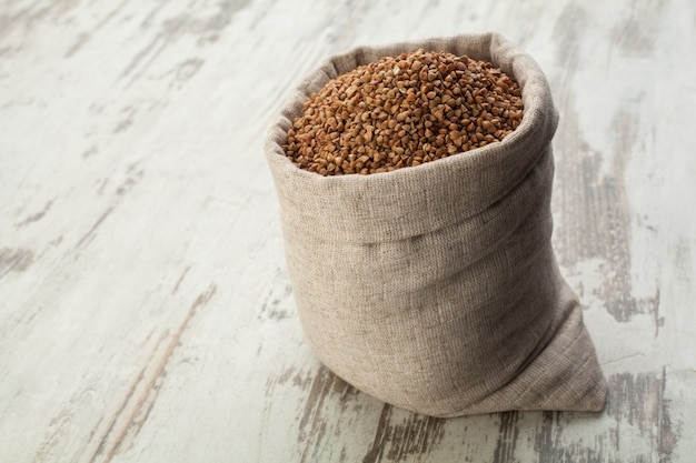 Sac en lin plein avec du sarrasin dans un platelage en bois.