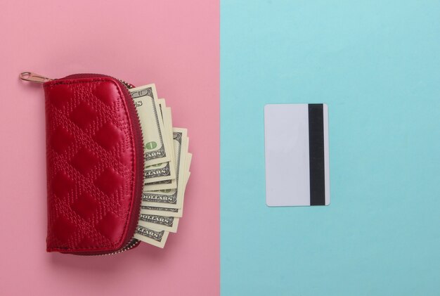 Sac à main rouge avec billets de cent dollars et une carte bancaire sur un pastel bleu-rose.