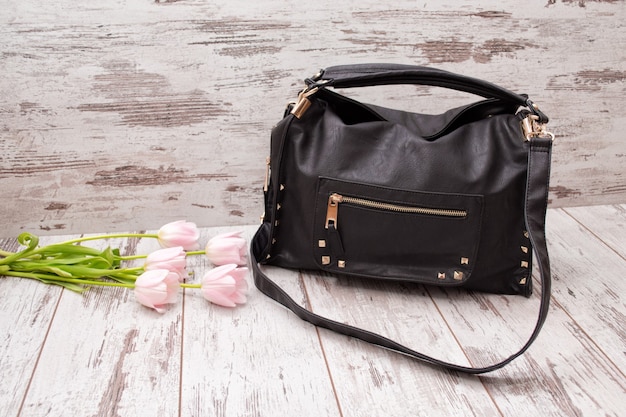 Sac noir sur fond de bois, tulipes roses