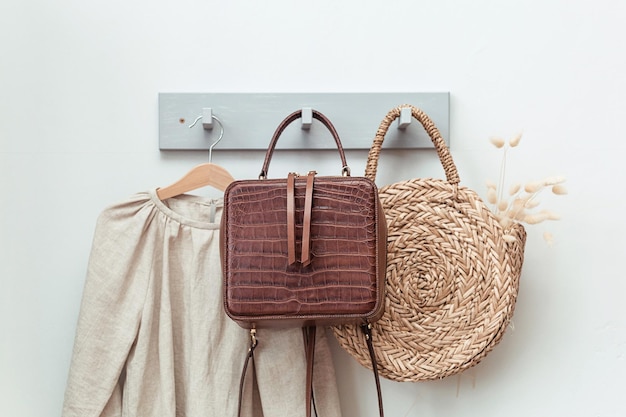 Un sac en paille élégant avec un beau bouquet et un sac à dos en cuir marron accroché à un mur gris à côté des vêtements