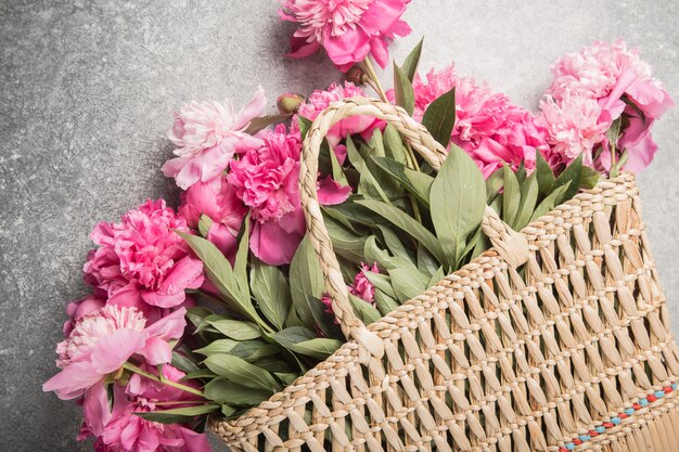 Sac de paille avec des fleurs de pivoine rose sur fond gris.