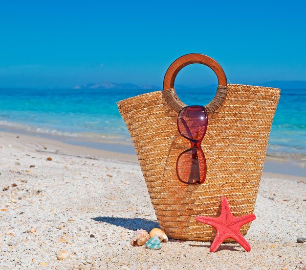 Sac de paille lunettes de soleil étoiles de mer et coquillages au bord de la mer