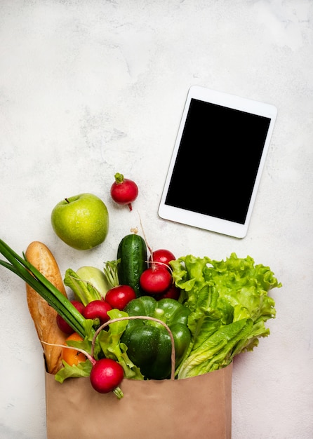 Sac en papier plein de produits alimentaires sains et tablette. Vue de dessus.