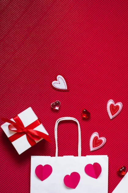 Sac en papier rouge, boîte cadeau blanche avec ruban de satin rouge et différents coeurs sur rouge