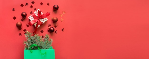 Sac en papier vert de Noël avec achats de cadeaux et de vacances sur rouge.