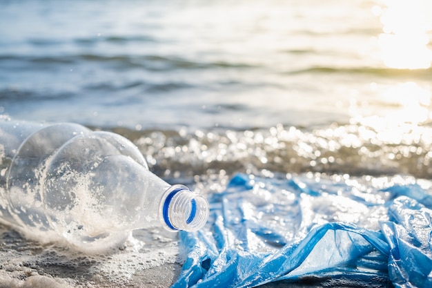 Sac en plastique et bouteilles sur la plage, le bord de mer et le concept de pollution de l'eau.