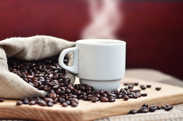 Un sac plein de grains de café brun et une tasse blanche de café chaud repose sur une surface en bois