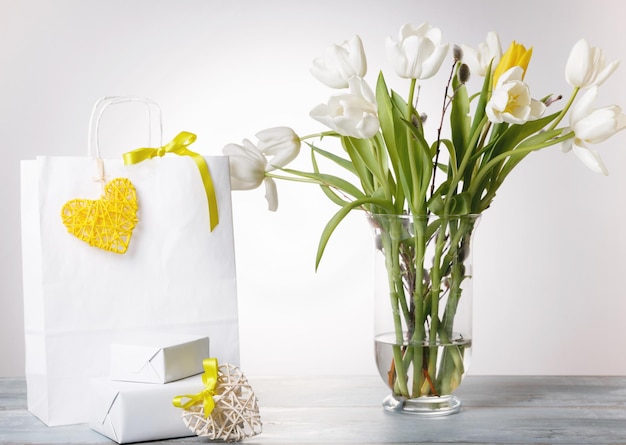 Photo sac à provisions coeur jaune et ruban cadeau et bouquet blanc bouquet de tulipes dans un vase sur fond blanc