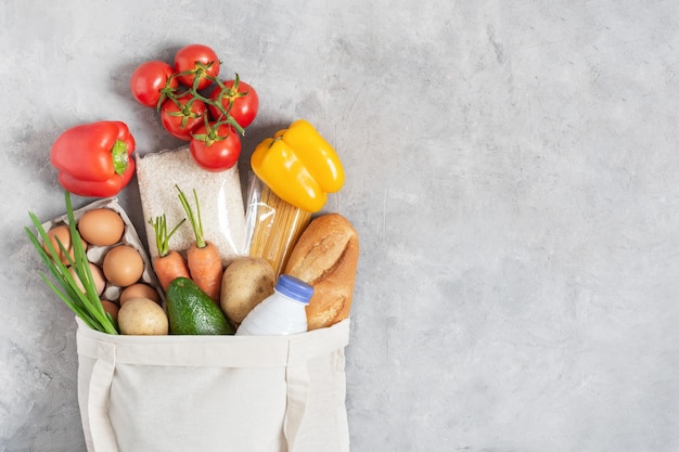 Sac à provisions écologique en coton rempli de légumes biologiques frais et de produits d'épicerie sur une table grise