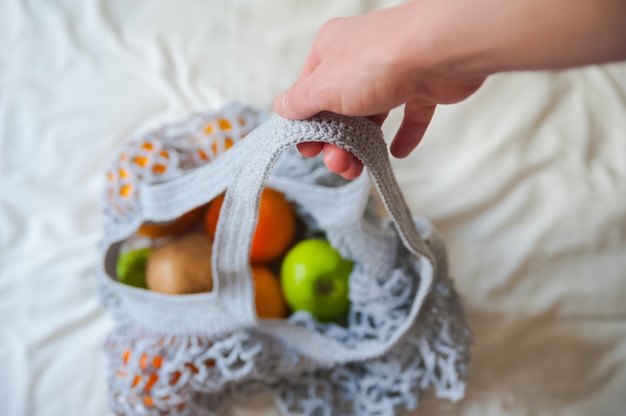 sac à provisions en filet avec oranges et pommes sur textile froissé.