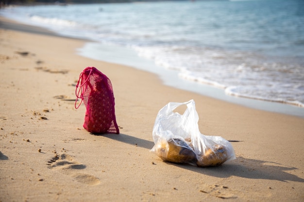 Un sac à provisions en filet et un sac en plastique se trouvent sur la plage de sable de la mer par une journée ensoleillée. concept d'écologie des océans